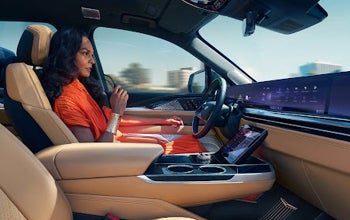 Two women seated in a lounge area having a conversation, one holding a tablet while the other holds a coffee cup.