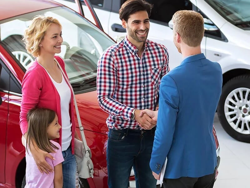 family shaking hands with sales manager as they trade their vehicle for a new one